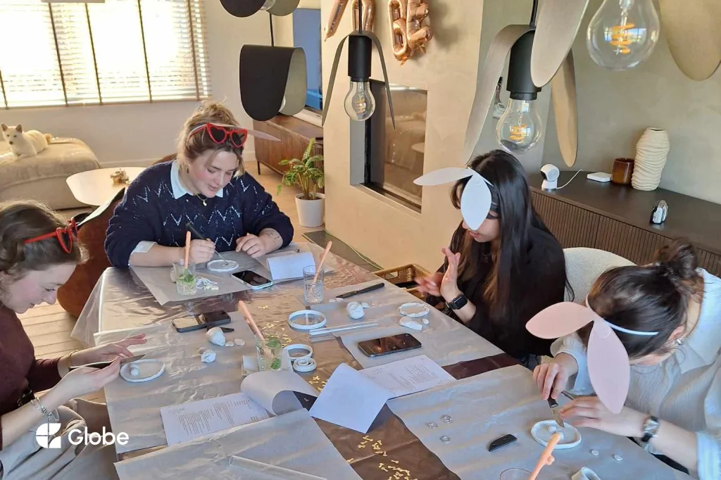 Bride and bridesmaids doing a pottery activity together during a bachelorette trip, with a bride balloon in the background