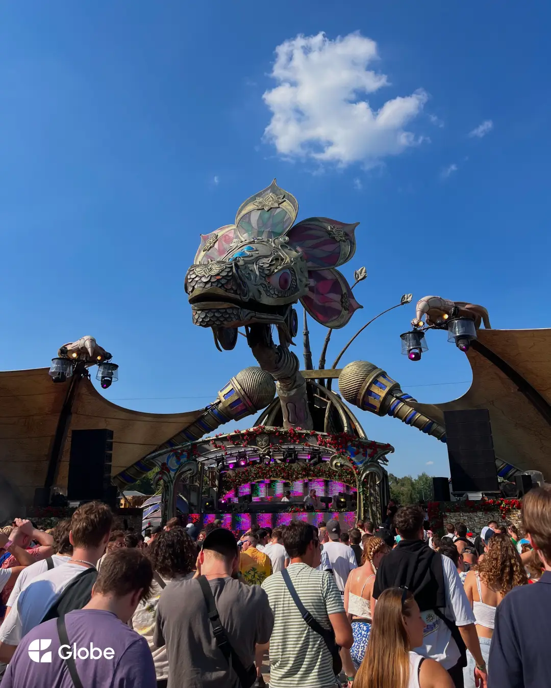 A crowd looking up at one of Tomorrowland's elaborate mainstage sculptures under a clear blue sky