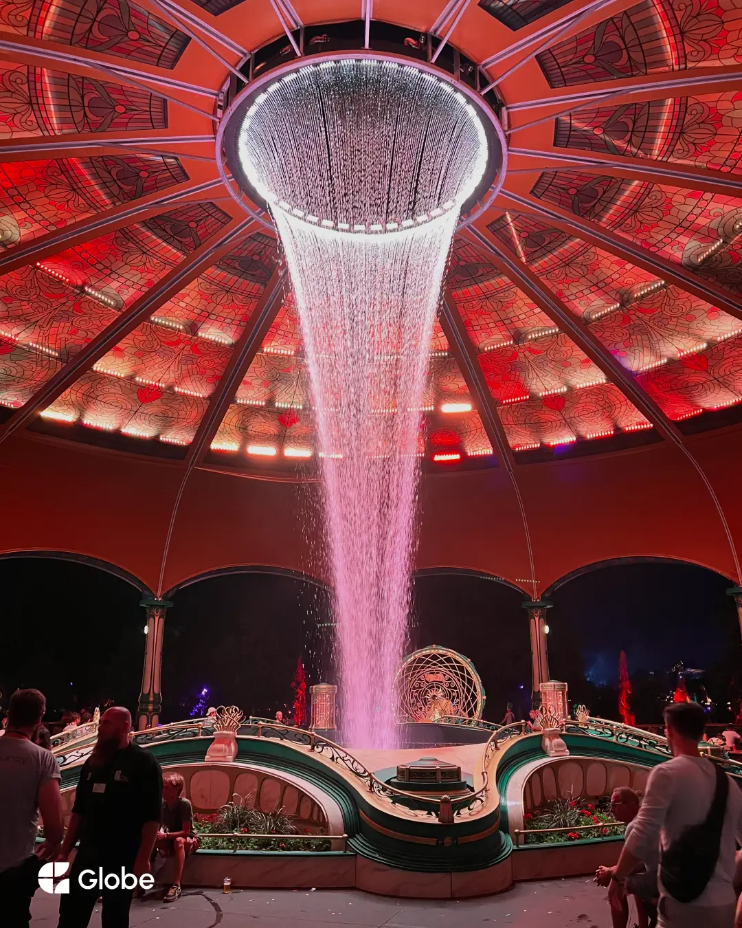 A pink light shower pouring from a domed stage ceiling at Tomorrowland at night