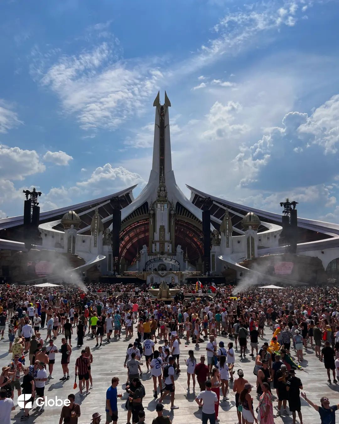 A massive daytime crowd gathered in front of Tomorrowland's mainstage under a bright blue sky