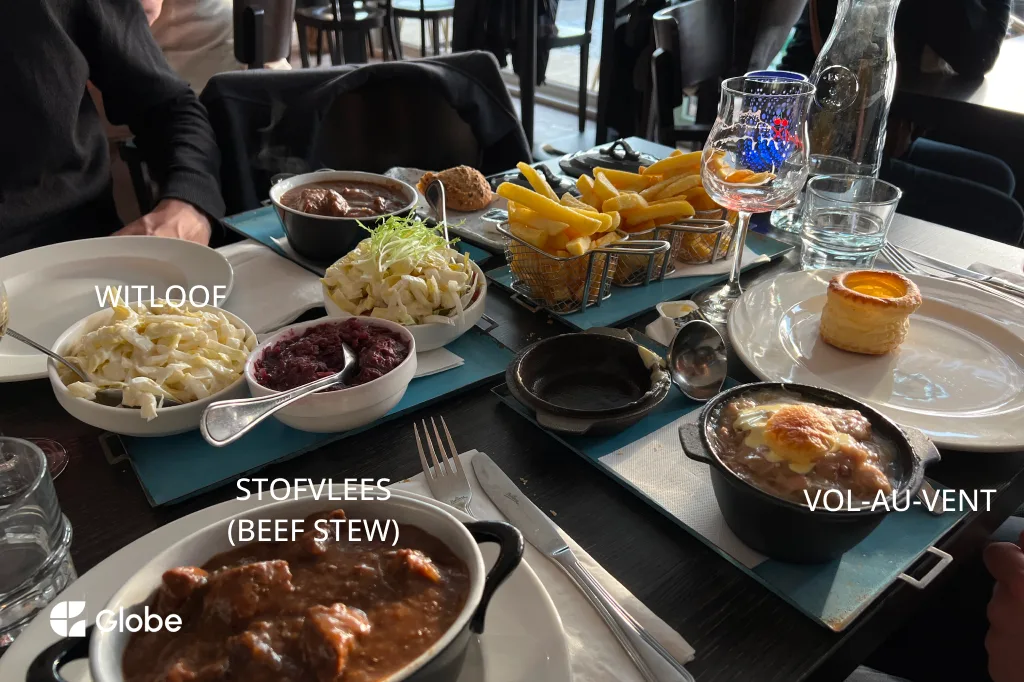 A Belgian food spread with stofvlees beef stew, witloof gratin, vol-au-vent, and a basket of fries