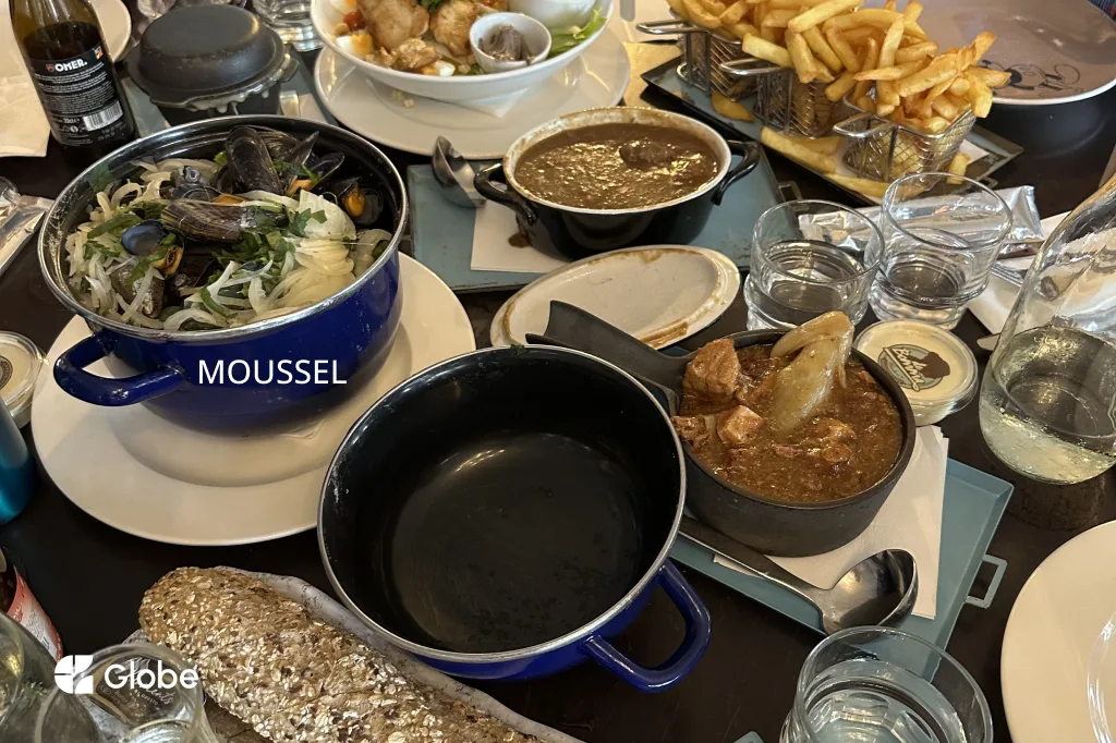 A pot of Belgian mussels alongside fries and stofvlees at a restaurant table in Antwerp