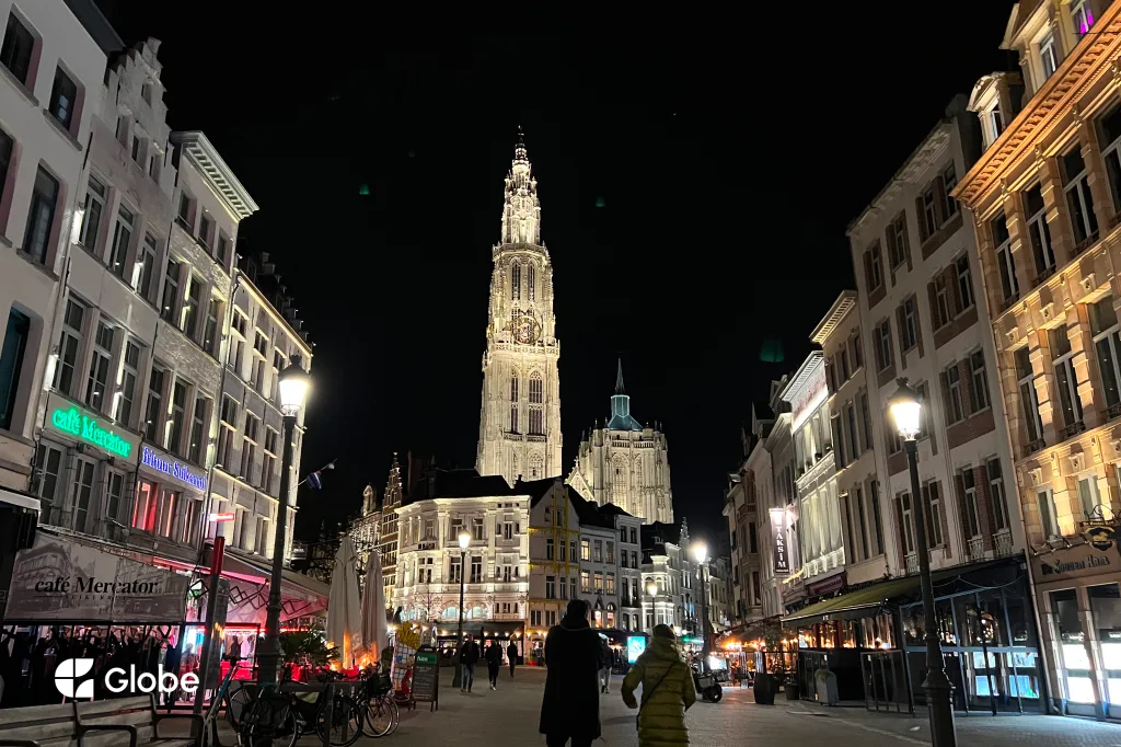 Antwerp's Grote Markt street at night, the Cathedral of Our Lady tower lit up in the distance