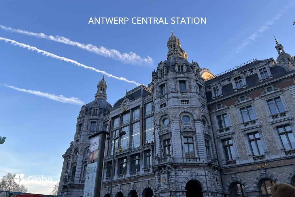 The ornate stone facade and domes of Antwerp Central Station under a blue sky
